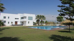 A modern building with a swimming pool, surrounded by grass and palm trees.