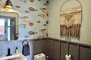 Baño con espejo, lavamanos, inodoro y decoración en la pared.