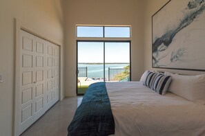 Ein Schlafzimmer mit einem großen Bett, Meerblick und einer Tür zu einem Balkon.