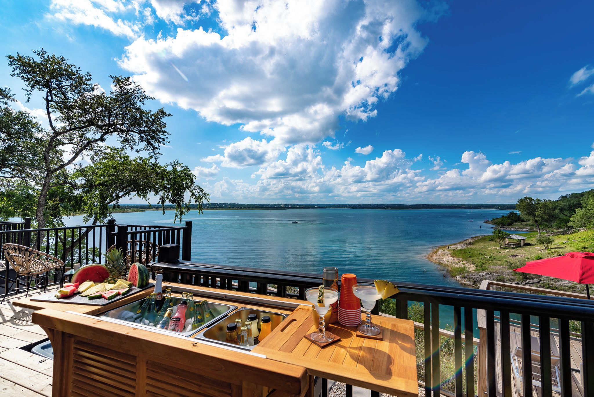 A wooden deck with a bar area, outdoor seating, and a view of a lake.