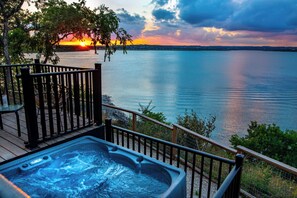 Ein Whirlpool auf einer Holzterrasse mit Blick auf einen See bei Sonnenuntergang.