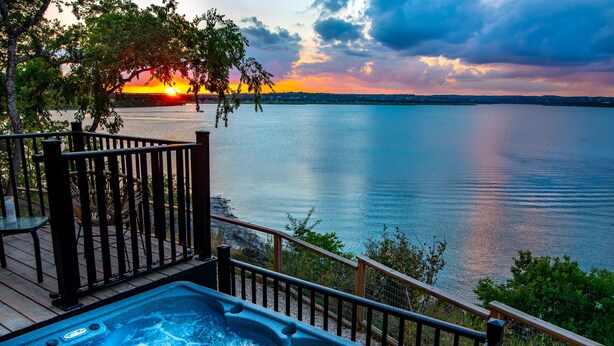 Ein Whirlpool auf einer Holzterrasse mit Blick auf einen See bei Sonnenuntergang.