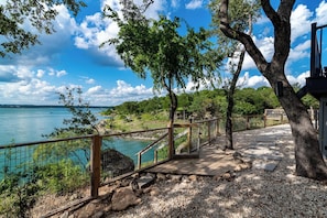 A wooden deck with a metal railing overlooking a body of water, surrounded by trees and pebbles.