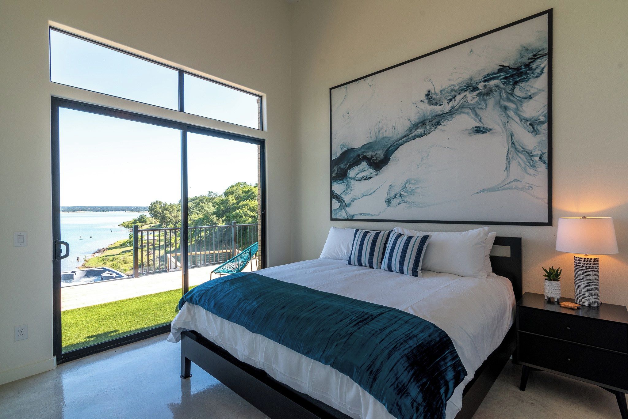 A bedroom with a large bed, a view of the outdoors, and a painting on the wall.