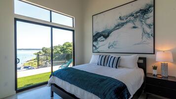 A bedroom with a large bed, a view of the outdoors, and a painting on the wall.