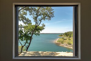A window view of a calm lake with trees and a distant shoreline. - Luxury Getaway - Waterfront, 4 BD, hot tub, stargazing. (Canyon Lake)