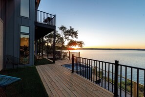 A deck with a hot tub, chairs, and a view of the sunset over water.