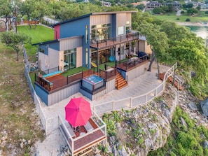 Una casa moderna de dos pisos con jacuzzi, mobiliario exterior y una terraza con vistas a una zona rocosa.