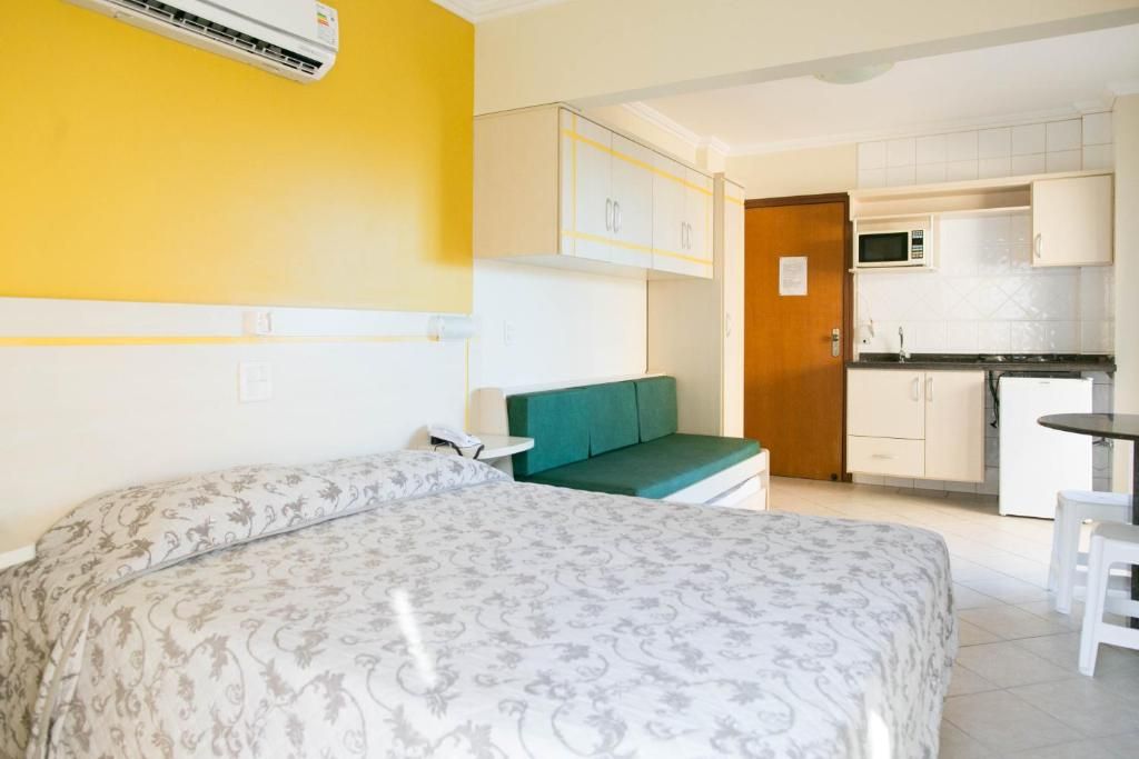 A hotel room with a bed, a green sofa, a small table, and a kitchenette area.