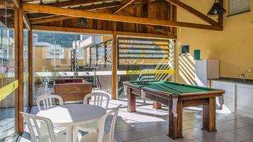 A billiards room with a pool table, chairs, and a kitchen area visible through glass doors.