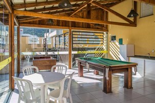 Una sala de billar con mesa de billar, sillas y una cocina visible a través de puertas de vidrio.