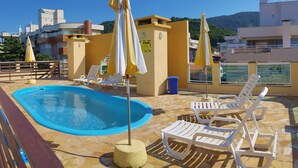 Un espace piscine aménagé sur le toit, comprenant une piscine, des chaises longues et des parasols.