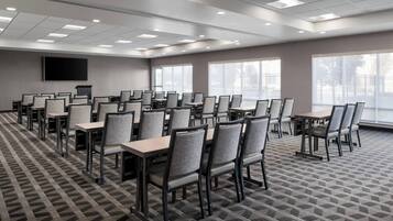 A conference room with multiple tables and chairs, large windows, and a flat-screen TV mounted on the wall.