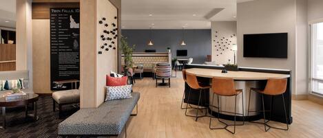 A modern hotel lobby with a bar area, seating, and a large wall-mounted TV.