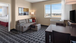 Quarto de hotel com cama, sofá, mesa de jantar, televisão e janela com vista para a cidade.