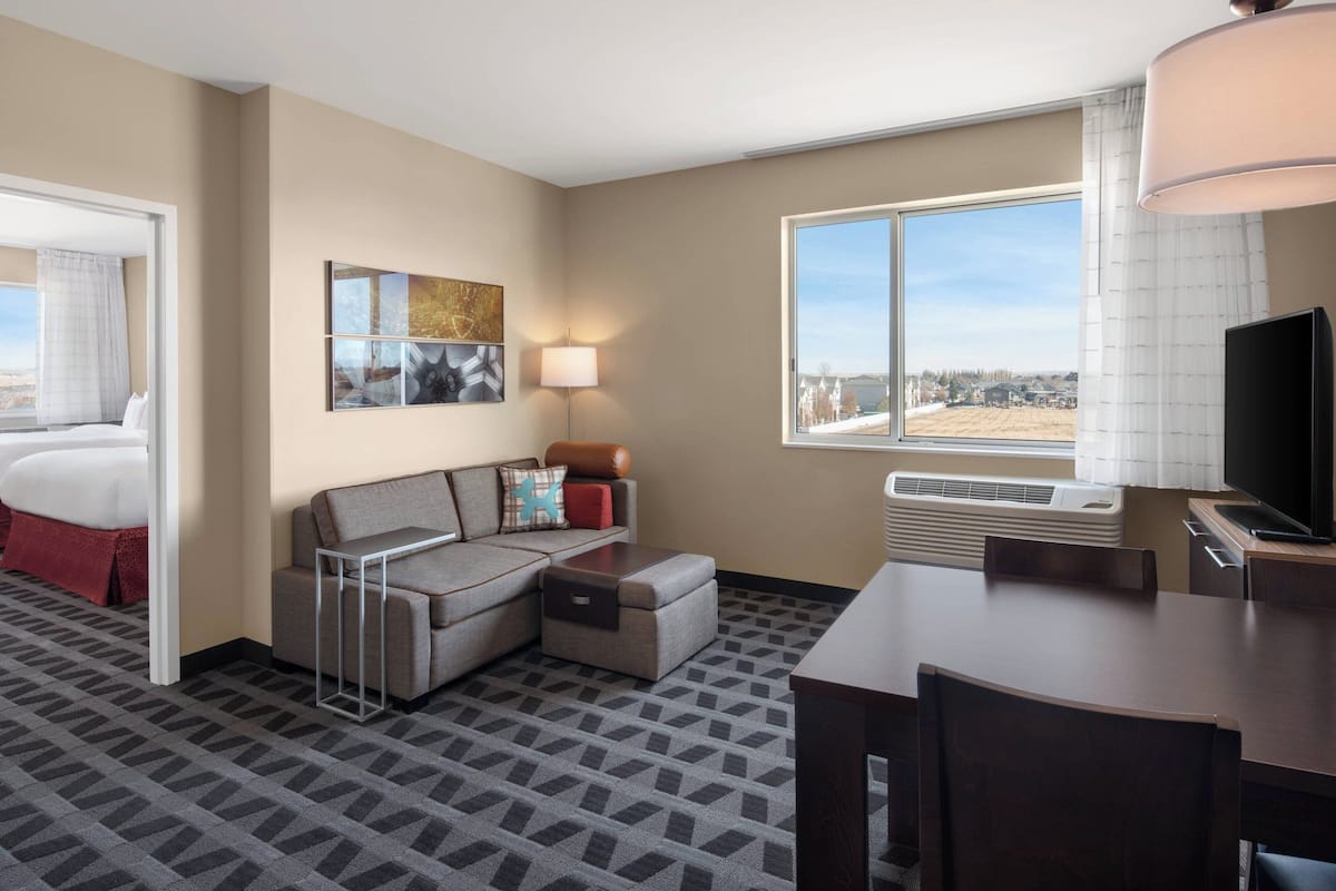 Hotelkamer met een bed, een sofa, een eettafel, een televisie en een raam met uitzicht over de stad.