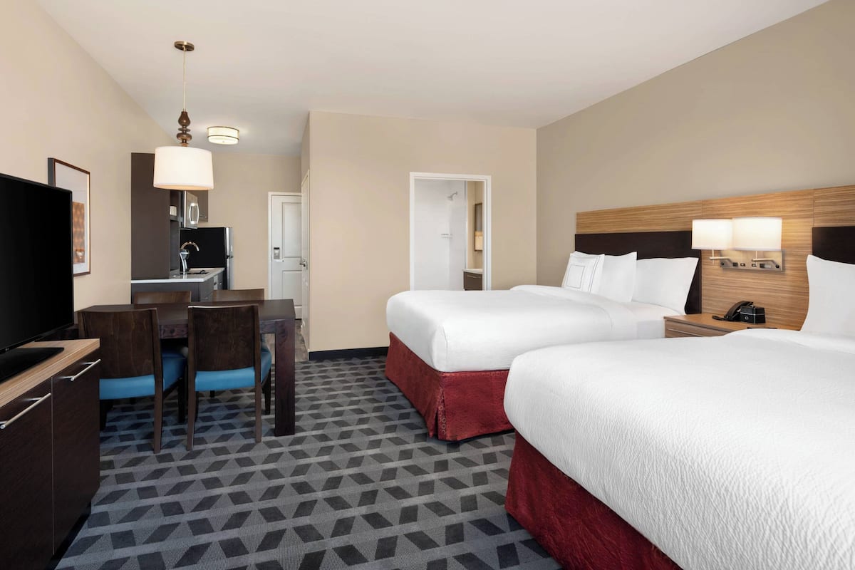 Een hotelkamer met twee bedden, een bureau, een televisie en een badkamer die door een geopende deur zichtbaar is.