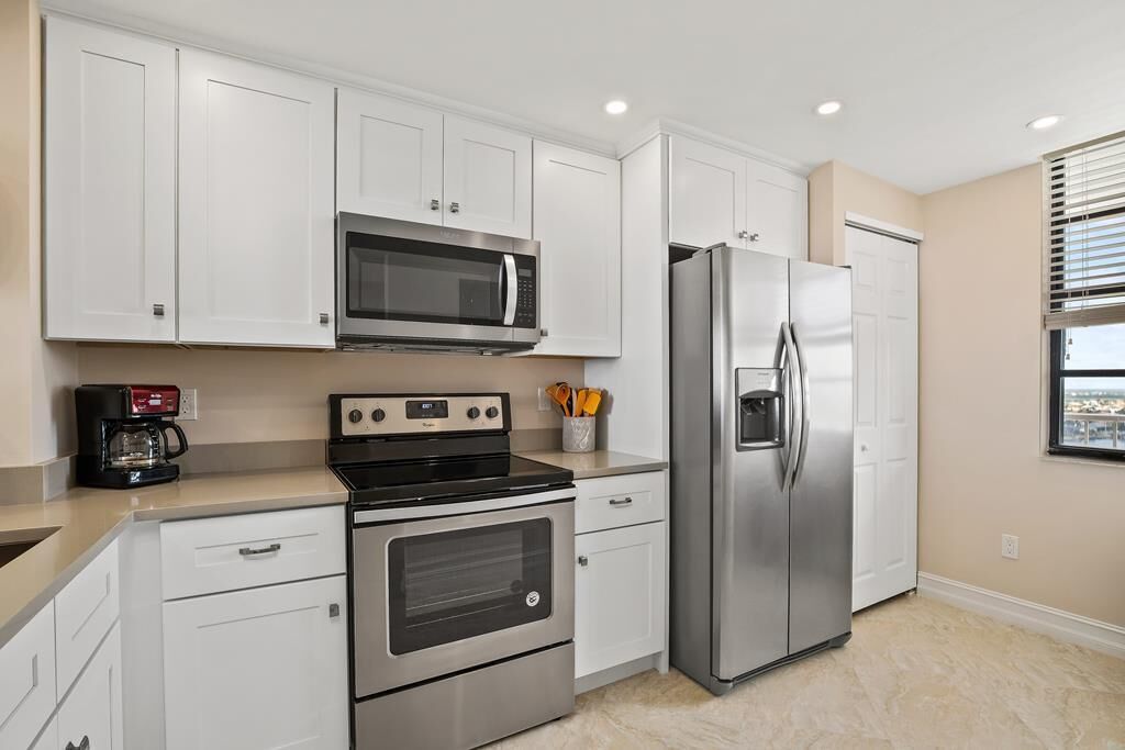 A modern kitchen with white cabinets, a stainless steel refrigerator, a microwave, an oven, and a coffee maker.