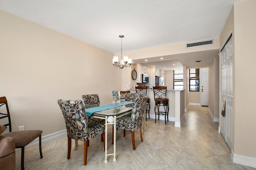 A dining area with a table and chairs, a chandelier, and a kitchen in the background.