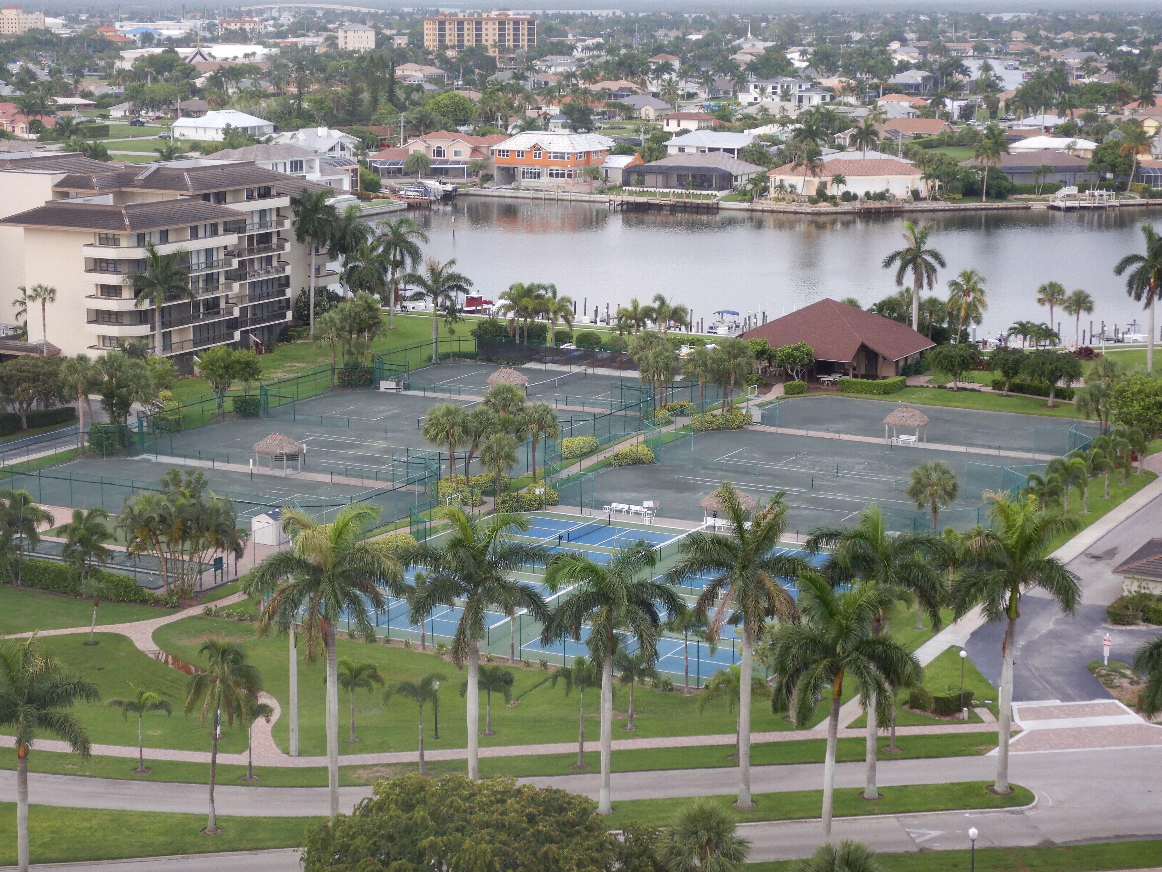 Una cancha de tenis rodeada de palmeras y un cuerpo de agua.