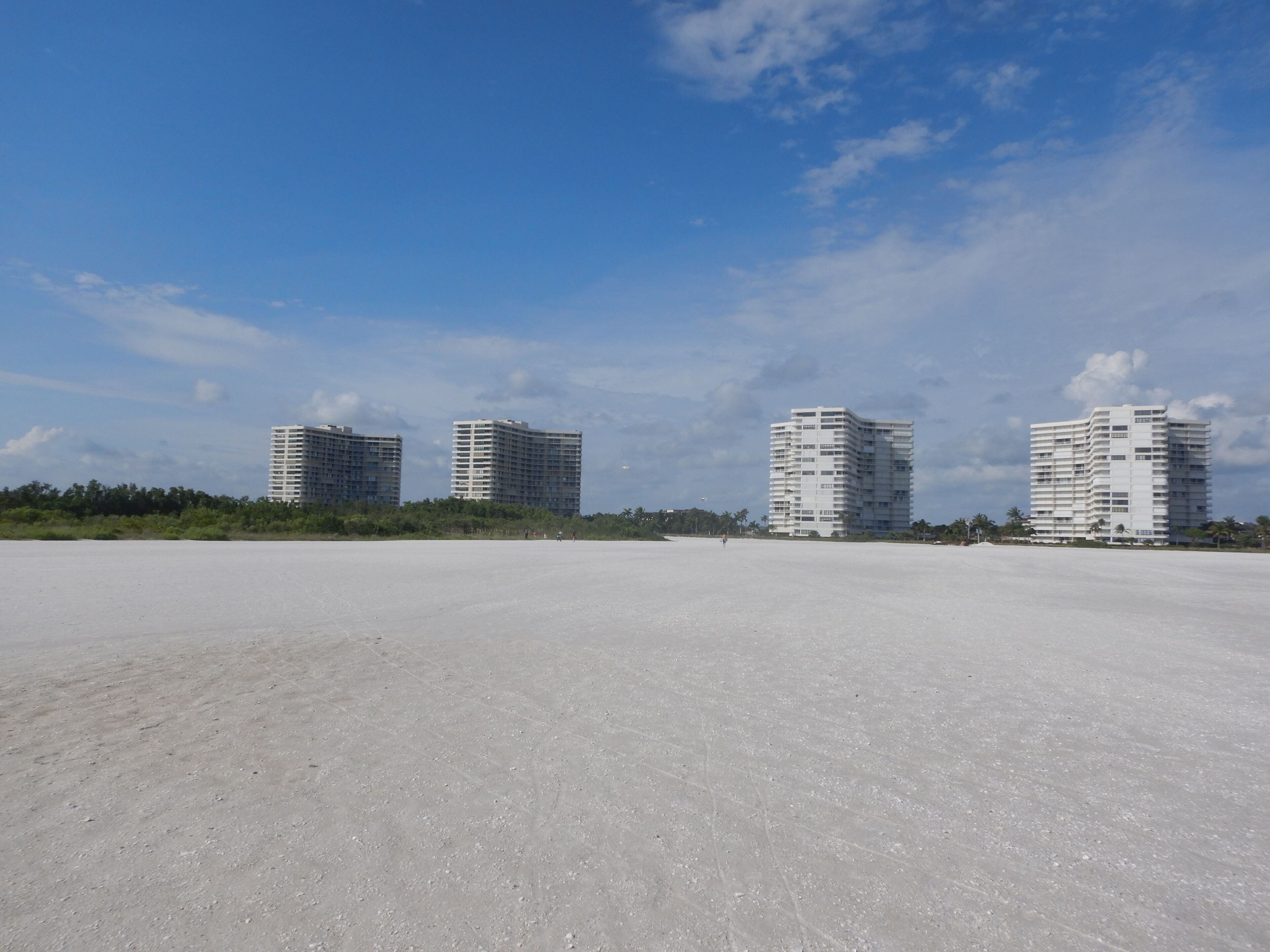 En kyststrækning med fire høje bygninger, en sandstrand og en klar himmel.