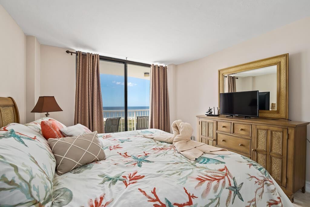 Habitación de hotel con cama, televisor, cómoda y vista al mar.