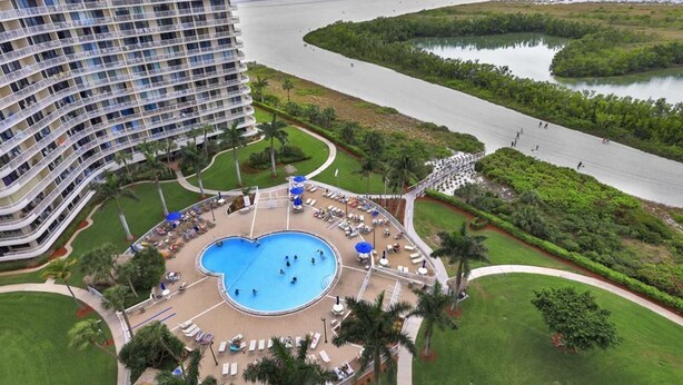 Um hotel com uma piscina grande, rodeada por espreguiçadeiras e palmeiras, com vista para uma praia e o mar.