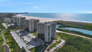 Hotel alto com vista para a praia, estacionamento e área ajardinada.