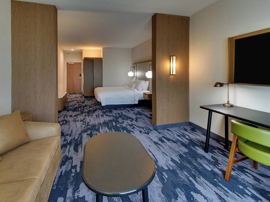 A hotel room with a bed, a desk, a chair, a sofa, and a carpeted floor.