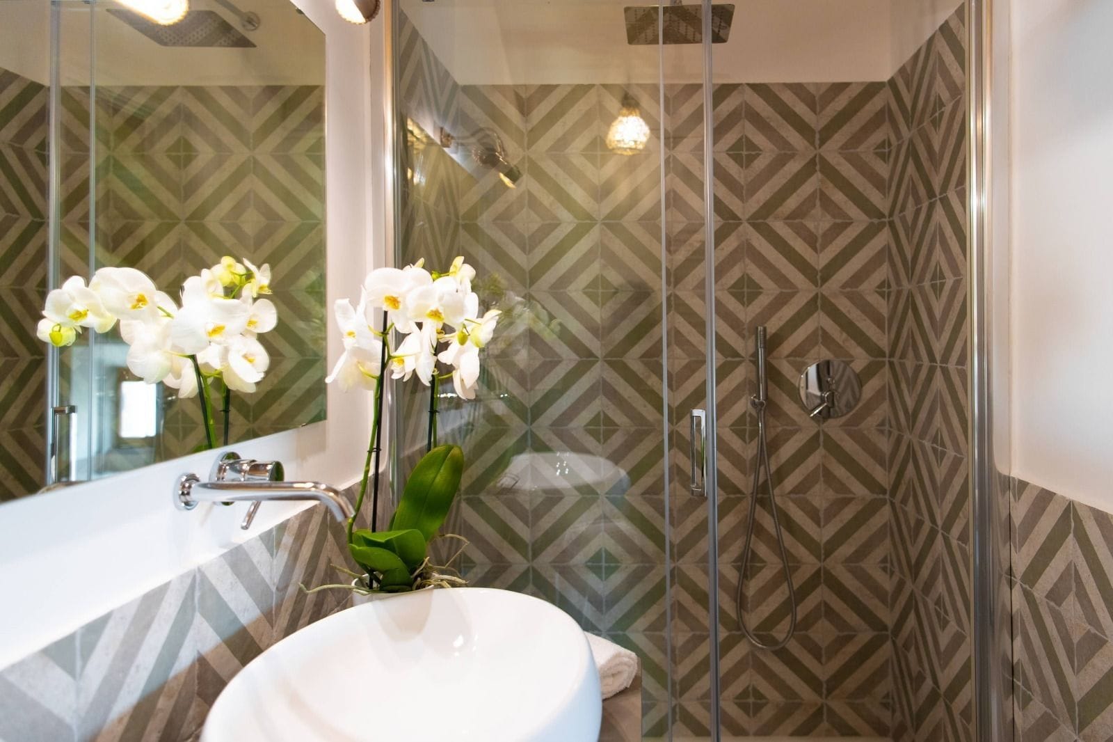 A bathroom with a glass shower enclosure, a white sink, and a mirror.