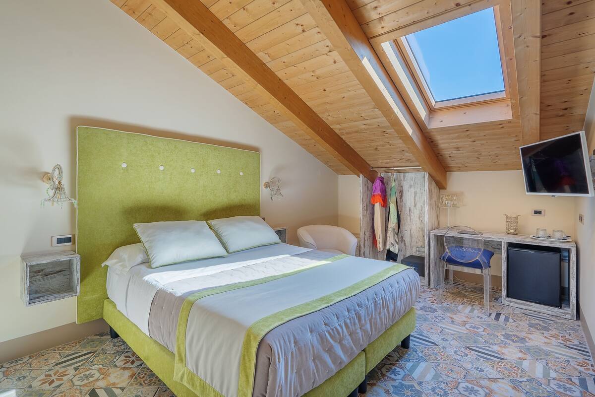 A bedroom with a bed, a desk, a television, and a skylight.