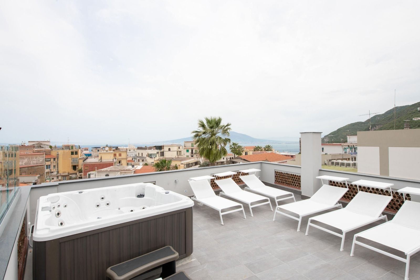 A rooftop terrace with a hot tub, white lounge chairs, and a city view.