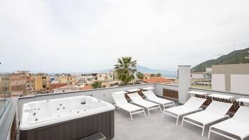 A rooftop terrace with a hot tub, white lounge chairs, and a city view.