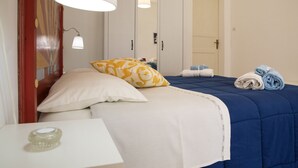 A neatly made bed with a blue comforter and white pillows, a bedside table with a candle, and a mirror above a wardrobe. - Bella Vista b&b (Erice)