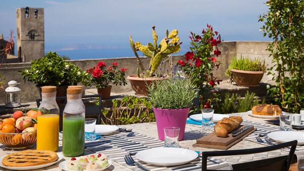 A table set for breakfast with a view of the sea, including a variety of fruits, drinks, and bread. - Bella Vista b&b (Erice)