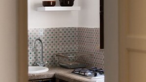 A kitchen with a sink, stove, and shelves above the counter. - Bella Vista b&b (Erice)
