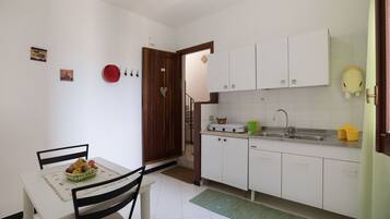 A small, clean kitchen with white cabinets, a sink, and a dining area with a table and chairs.