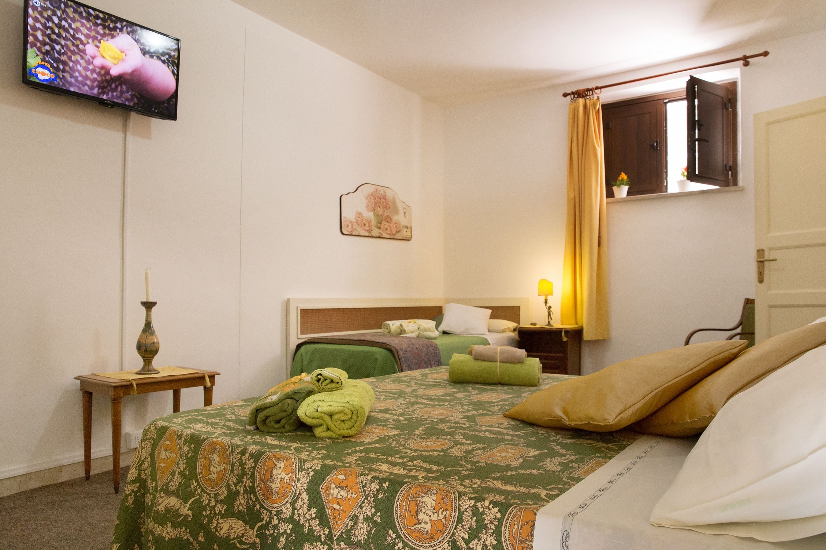 A hotel room with a bed, a television, a window with curtains, and a bedside table with a lamp.