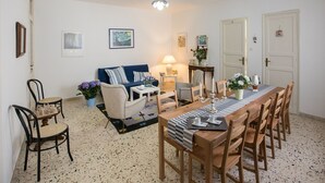 A dining area with a long wooden table, chairs, a blue sofa, and a small side table with a lamp. - Bella Vista b&b (Erice)