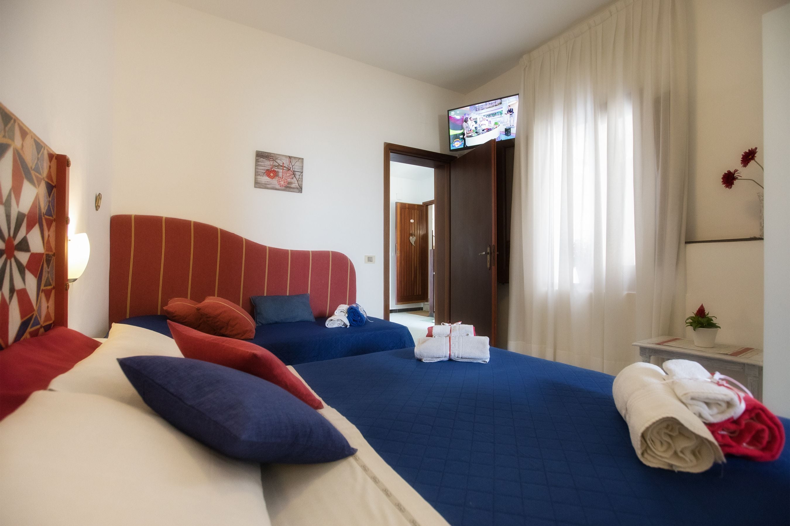 Une chambre d’hôtel avec deux lits, un téléviseur fixé au mur et une fenêtre avec des rideaux.