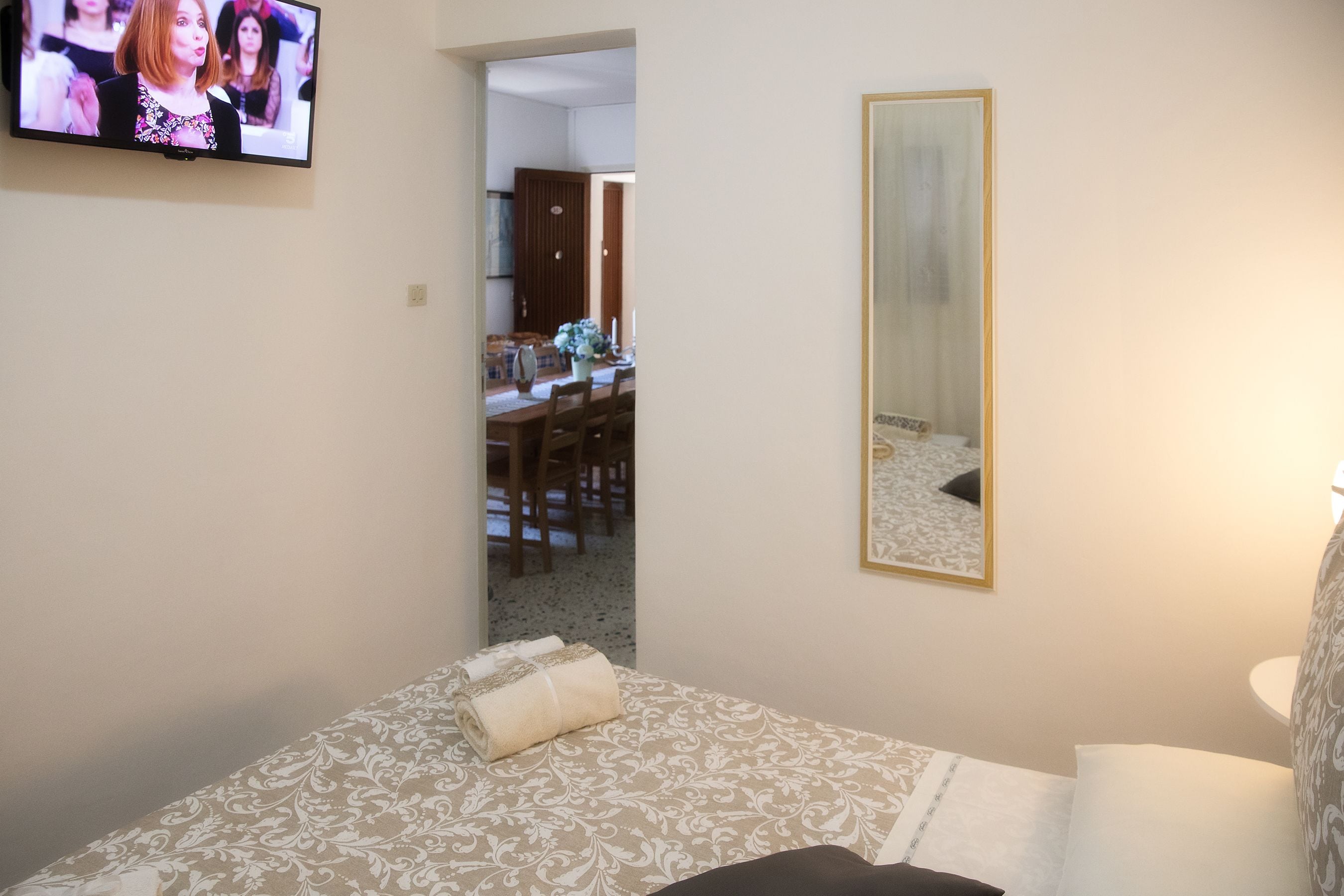 Une chambre d’hôtel avec un lit, une télévision, un miroir et un coin repas, le tout visible à travers une porte ouverte.