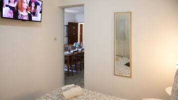 Una habitación de hotel con cama, televisión, espejo y un área de comedor visible a través de una puerta abierta.