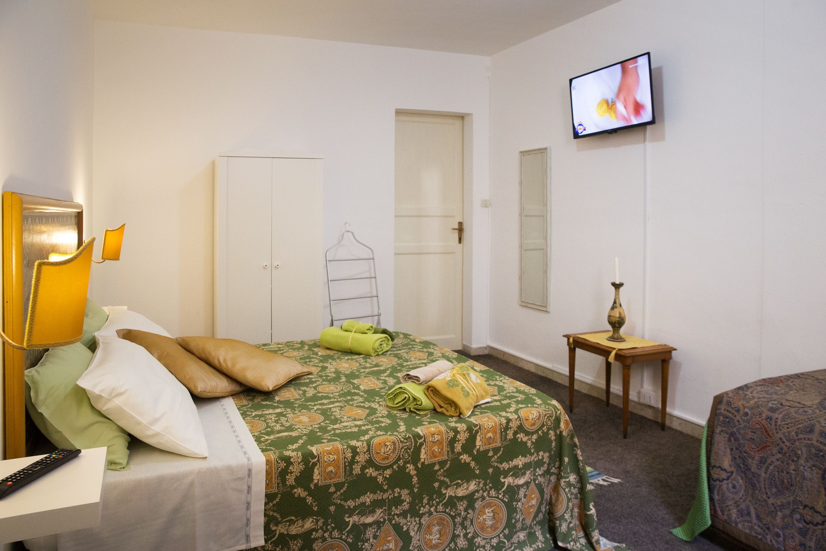 A hotel room with a bed, a television, a wardrobe, and a small table with a vase.