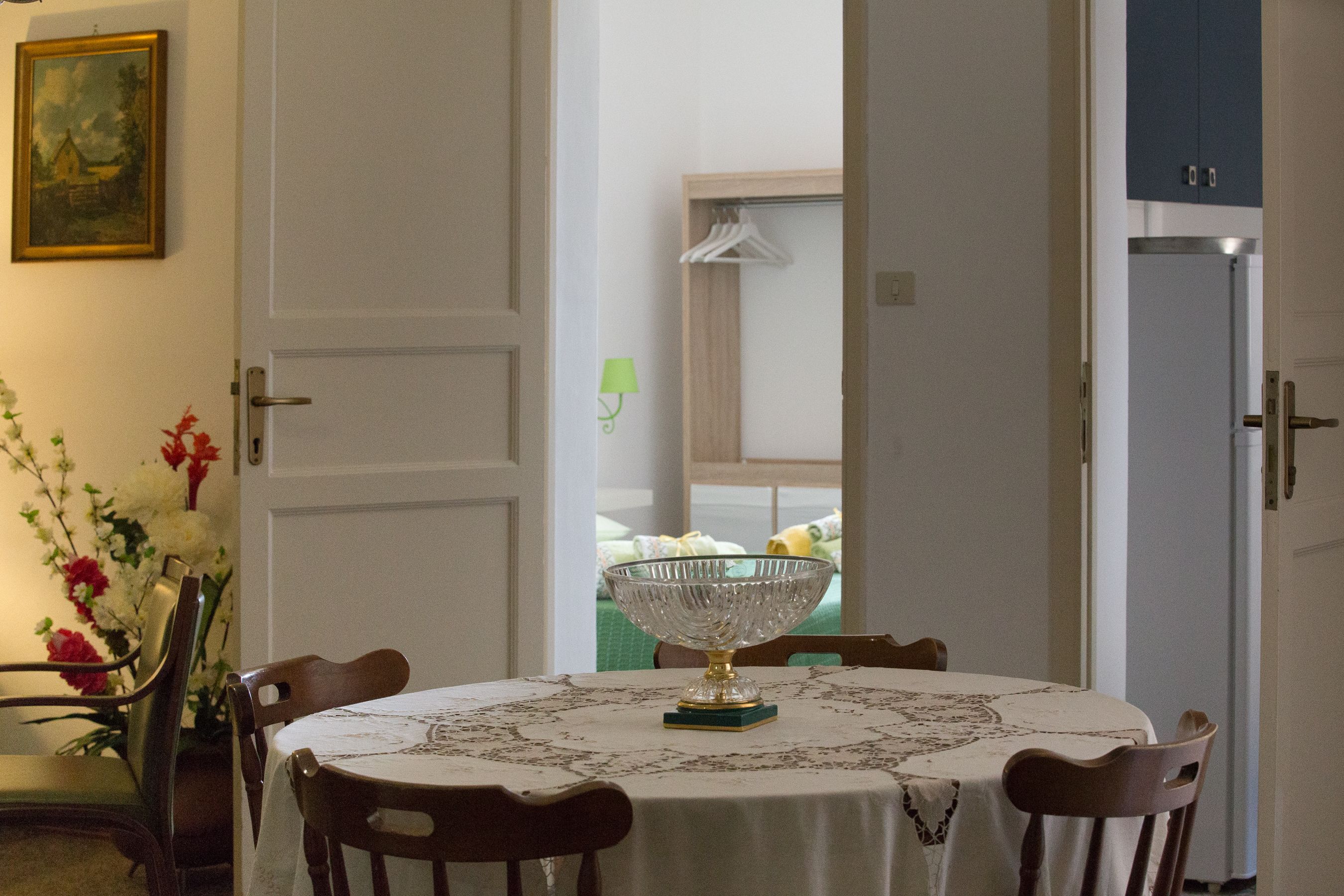Un coin repas avec une table dressée pour quatre personnes, un vase de fleurs et un tableau accroché au mur.