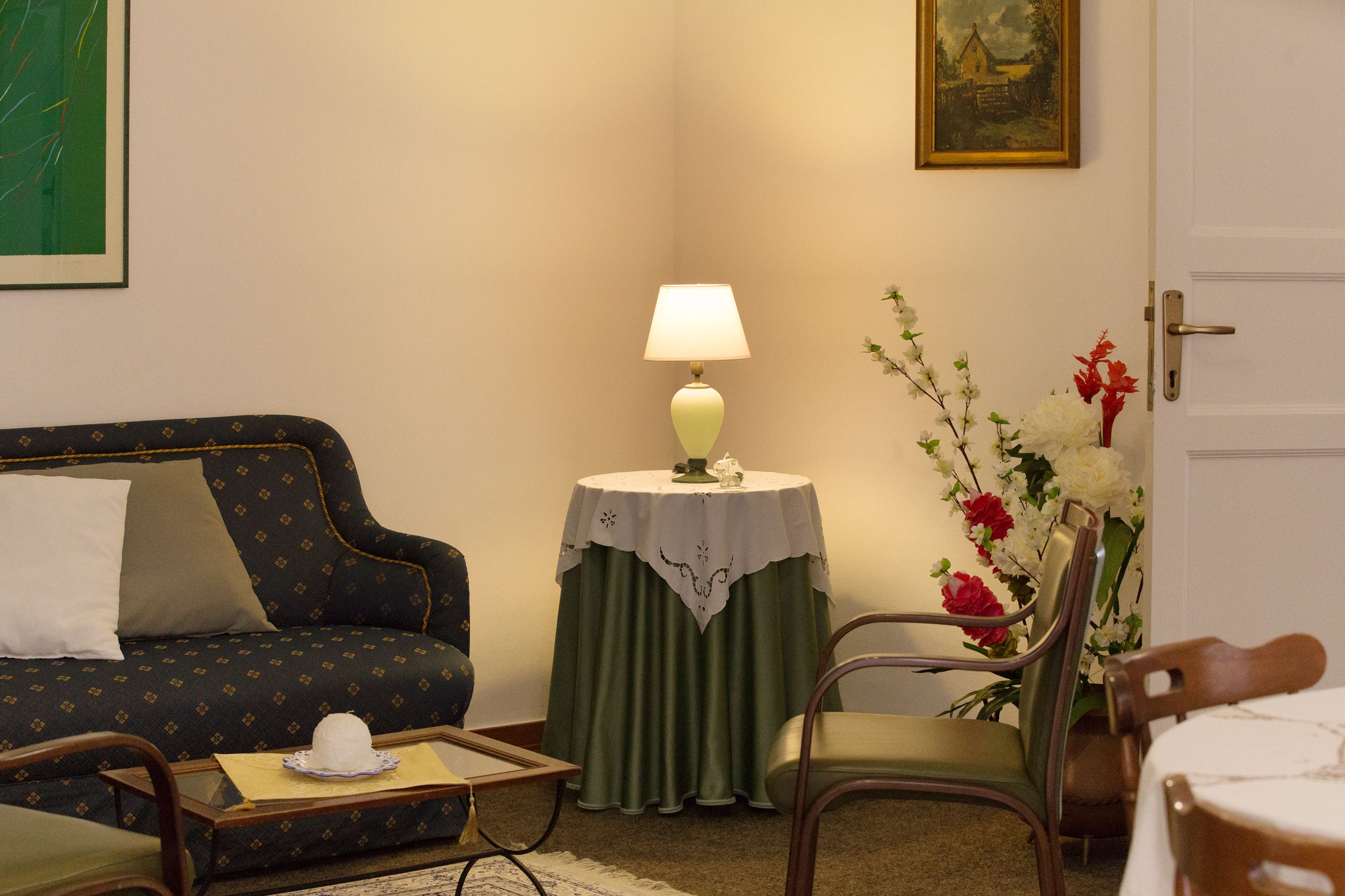 Un soggiorno con un divano, un tavolo con una lampada, una poltrona e un vaso con fiori.