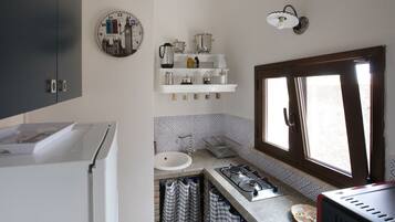 A compact kitchen with a sink, stove, and shelves above.