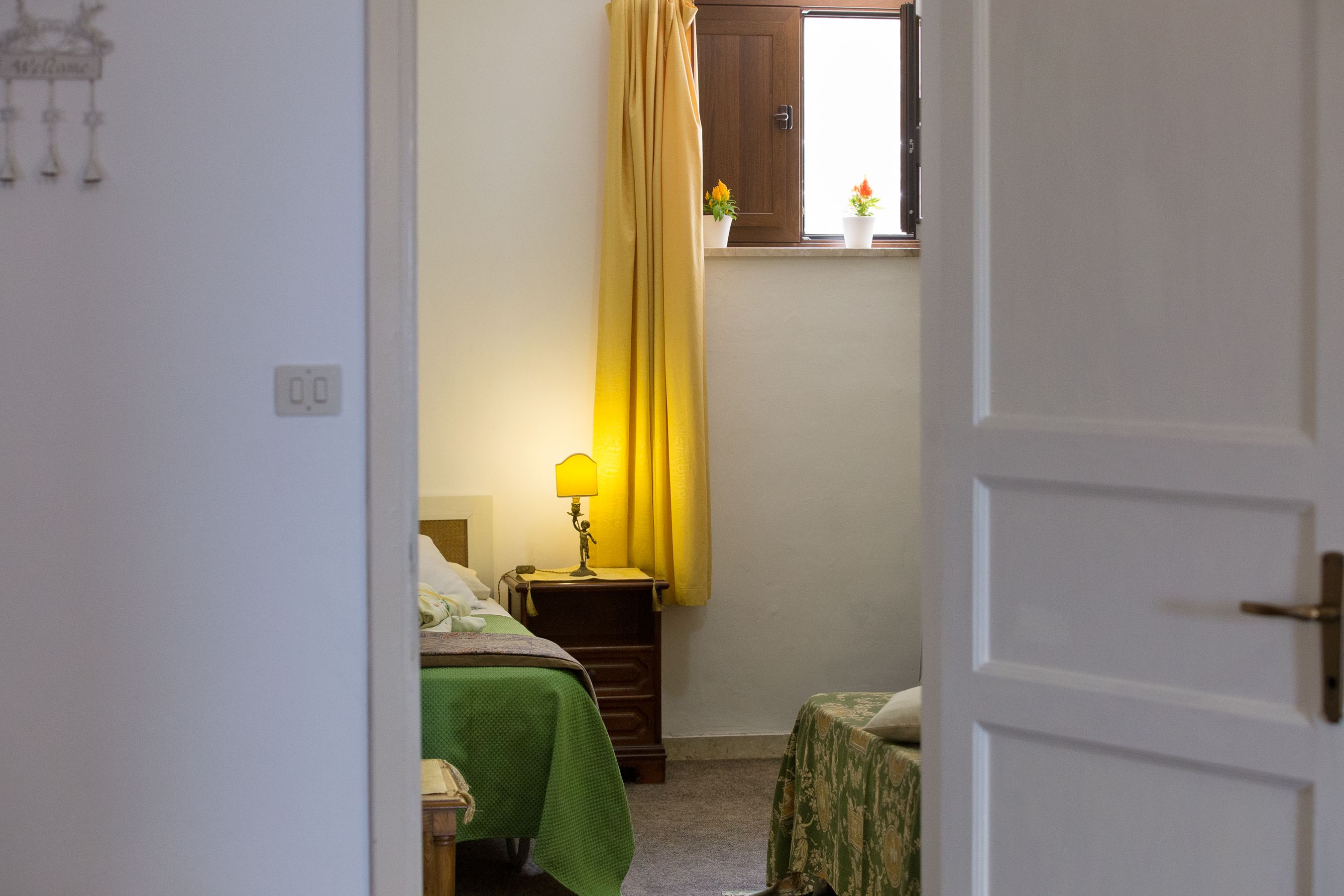 Une chambre à coucher avec un lit, une table de chevet avec une lampe, une fenêtre avec des rideaux et une petite table sur laquelle est posée une plante.
