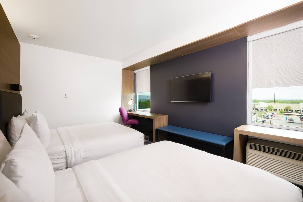 Habitación de hotel con dos camas, un escritorio, una silla, un televisor y una ventana con vistas a la ciudad.