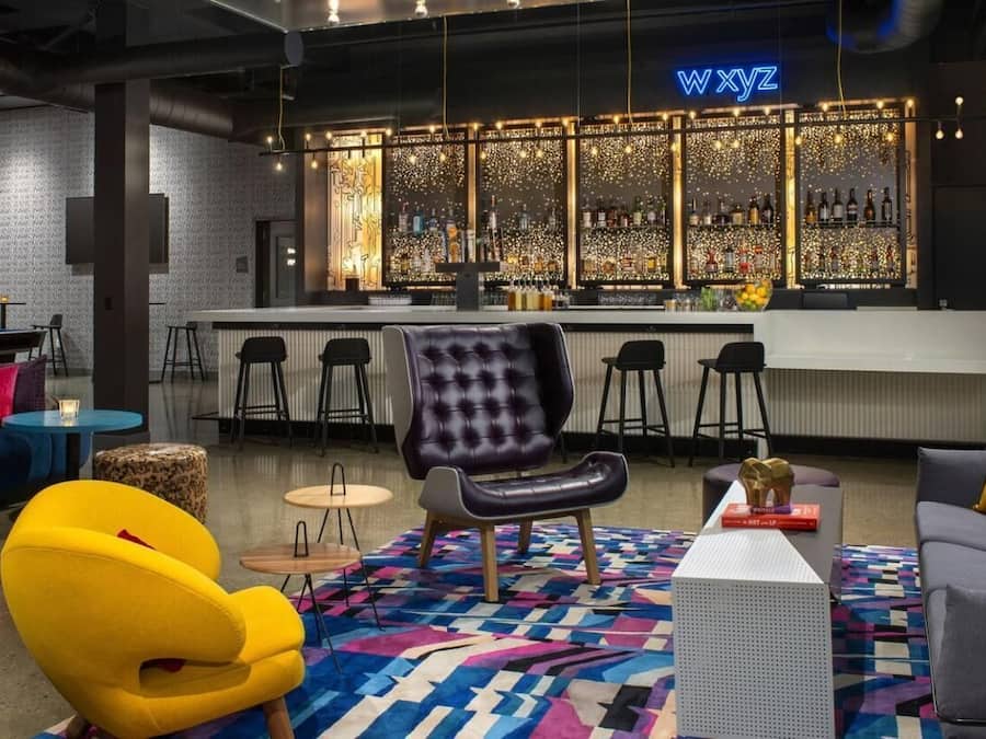 A modern bar area with a city view, bar stools, and a neon sign.