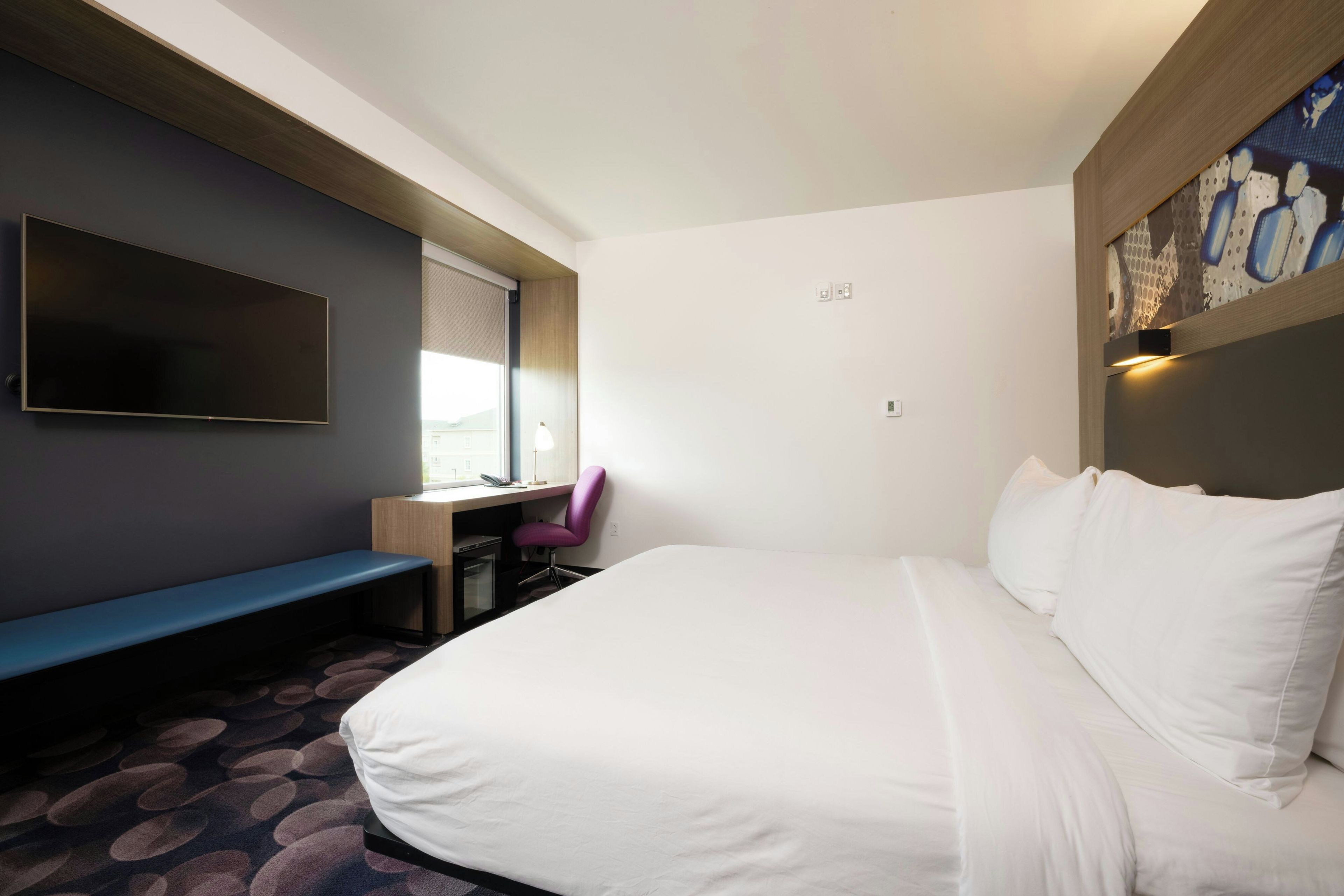A hotel room with a bed, a desk, a chair, a TV, and a window.